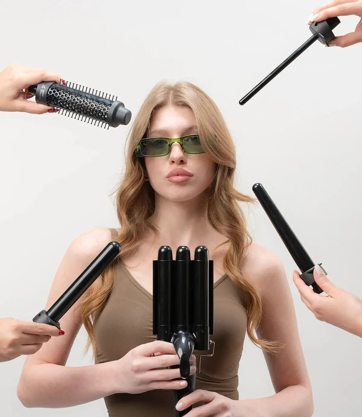 Woman with sunglasses surrounded by hair styling tools on a light gray background